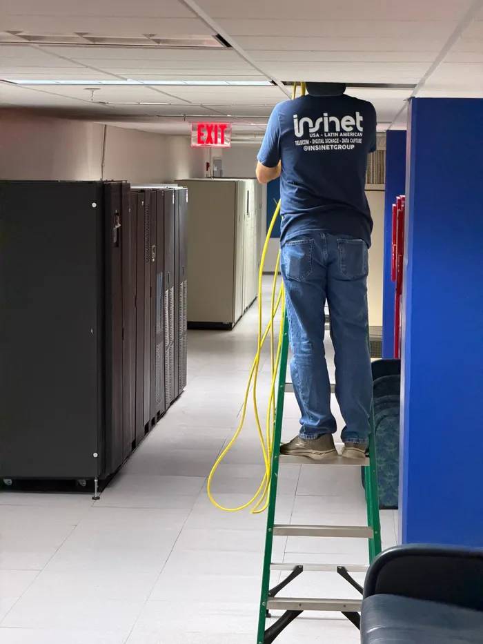 An Insinet technician on a ladder, pulling cable down a datacenter aisle.